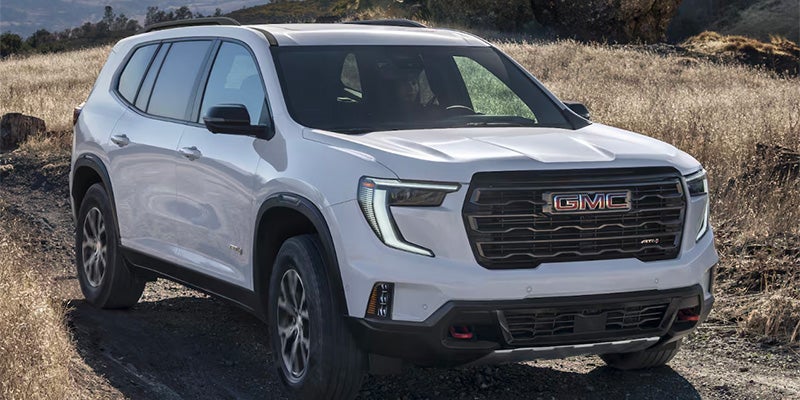 gmc-vehicle-2025-GMC-Acadia driving on muddy road surrounded by grass