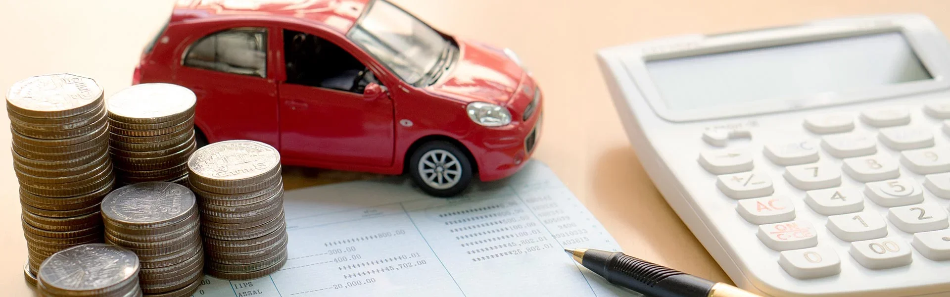Red toy car sitting on a desk with coins, paperwork, and a calculator